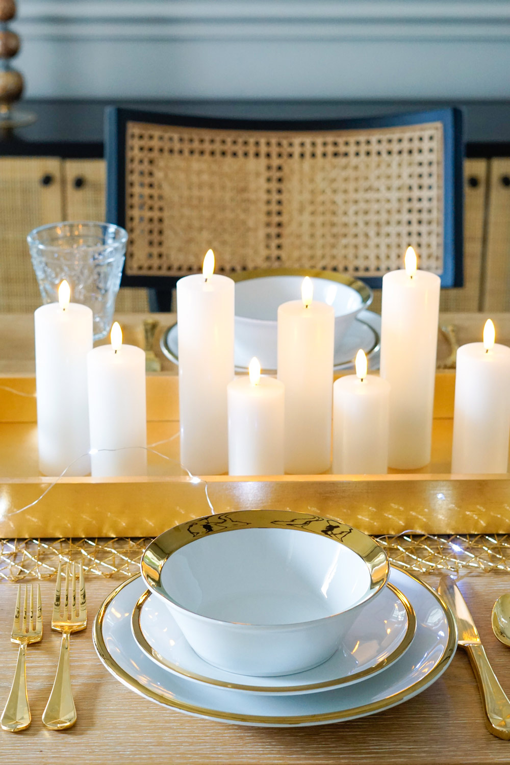 Table with a gold tray filled with candles in the center. White dinnerware with gold trim and gold flatware.