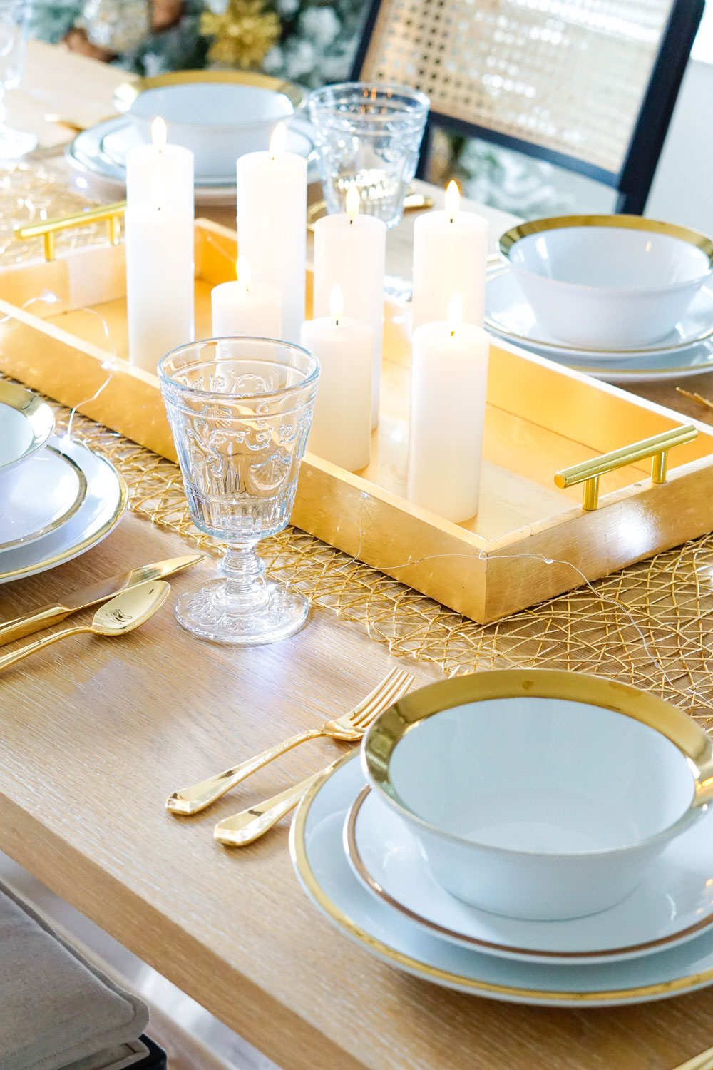 White dinnerware with gold trim, gold flatware, and glasses set up around a table.