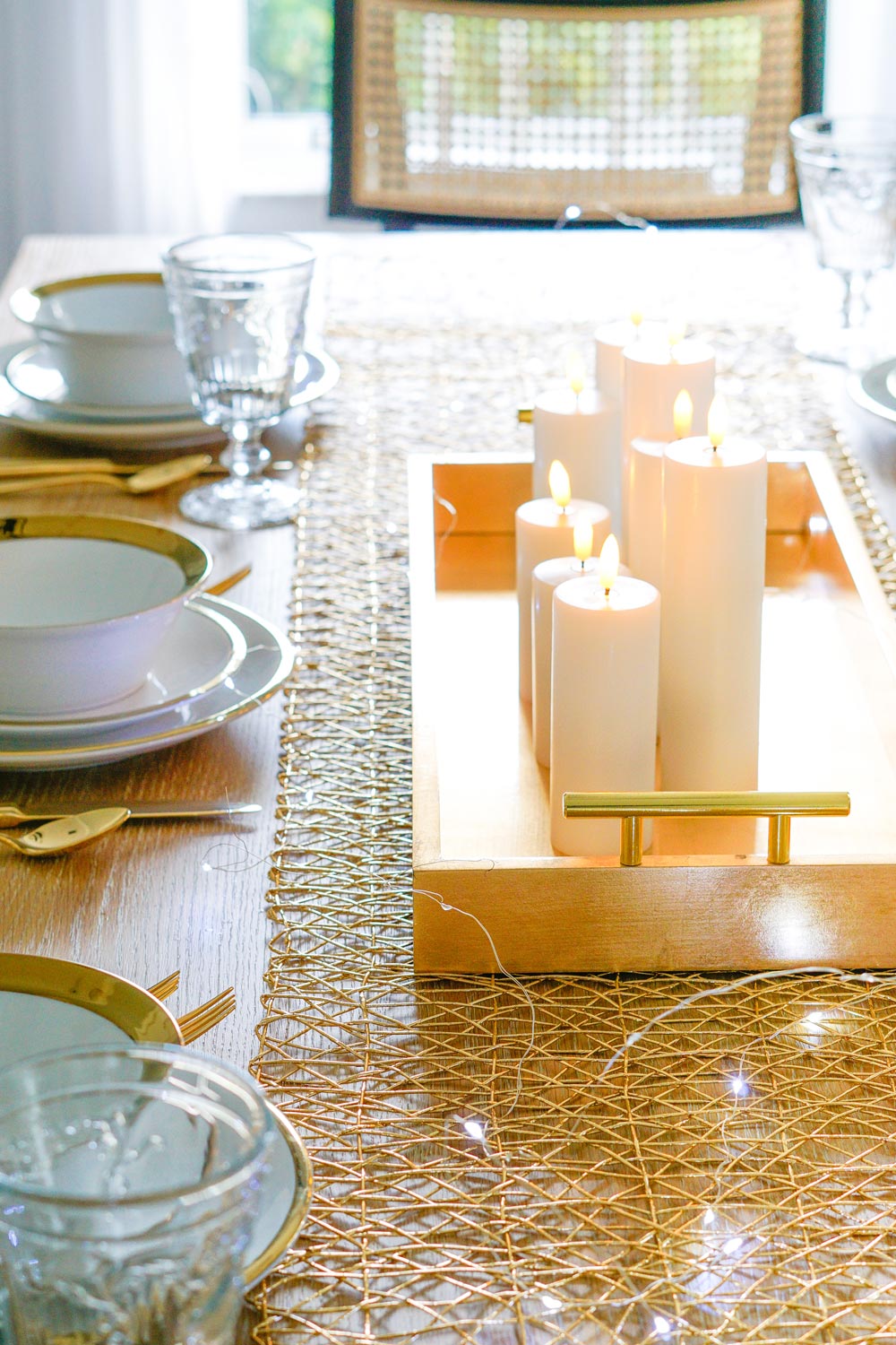 Table with a gold tray filled with candles in the center. White dinnerware with gold trim and gold flatware.