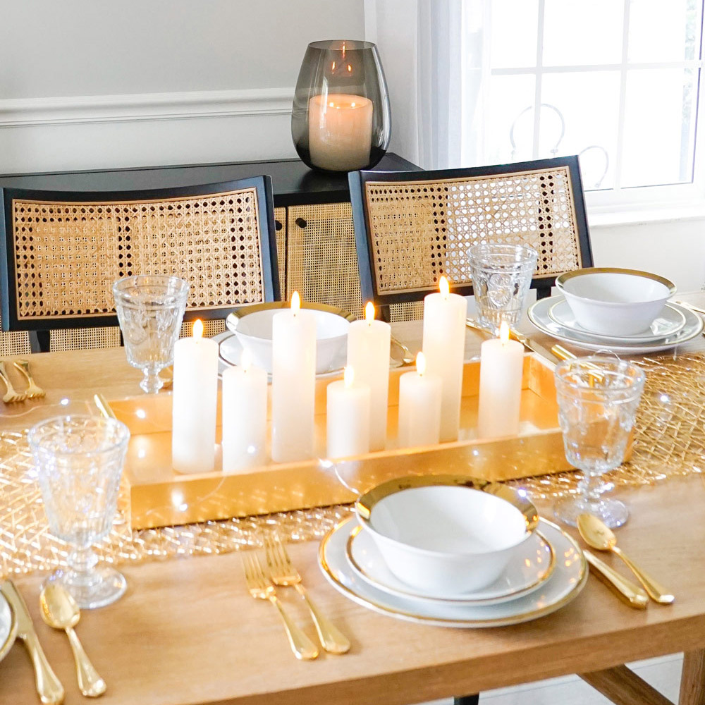 Table decorated with dinnerware, gold flatware, glasses, and a gold tray filled with candles.