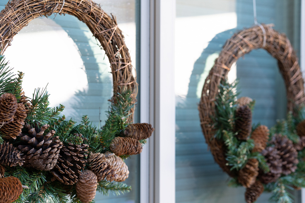 A window is styled with two wreaths adorned with pinecones