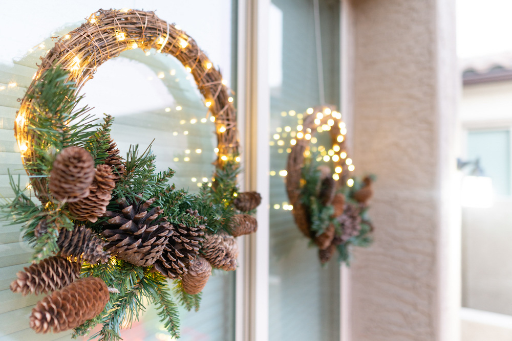 A window is styled with two illuminated wreaths adorned with pinecones 