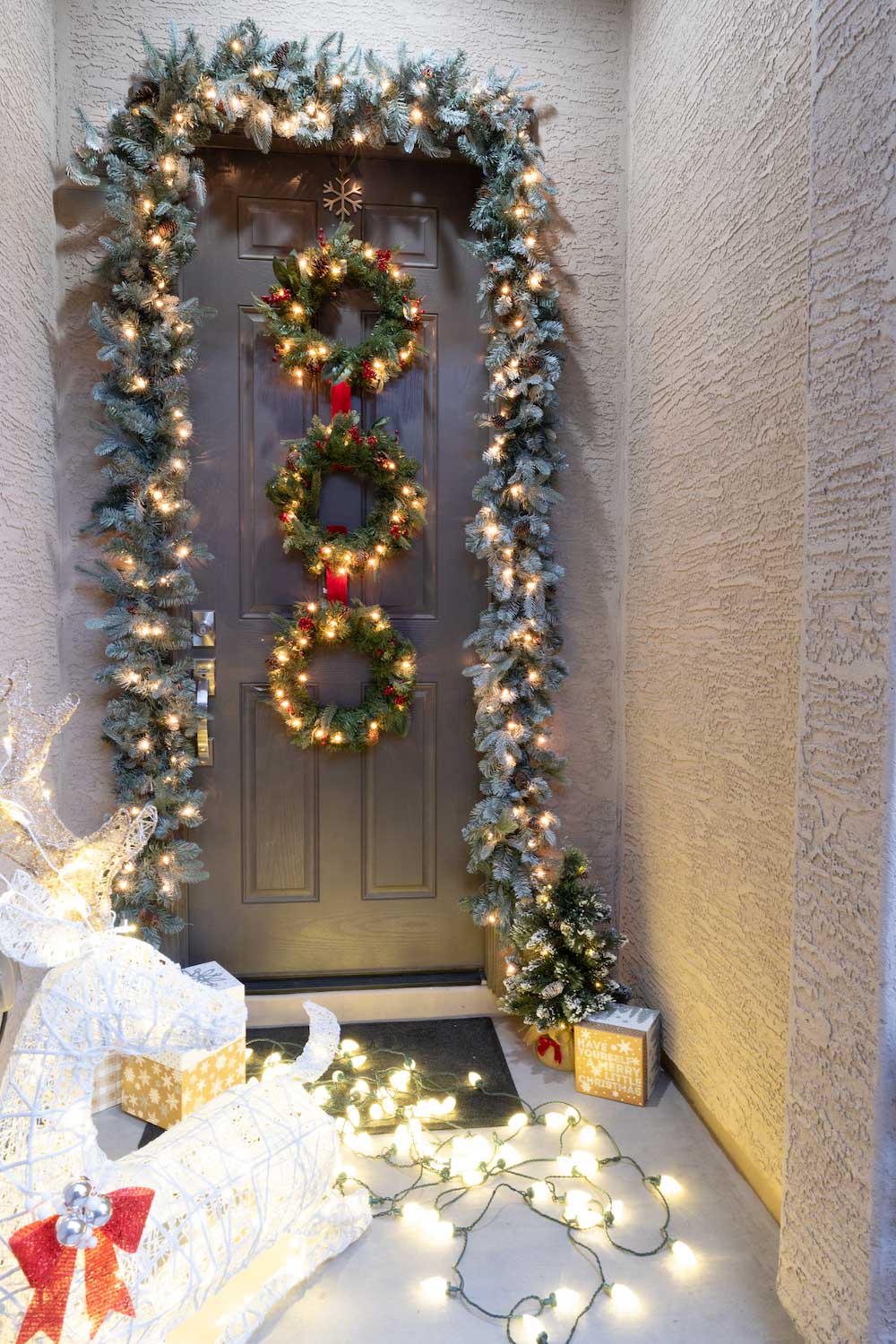 A front porch is styled with LED deer, presents, wreaths, garland, and a small tree at night