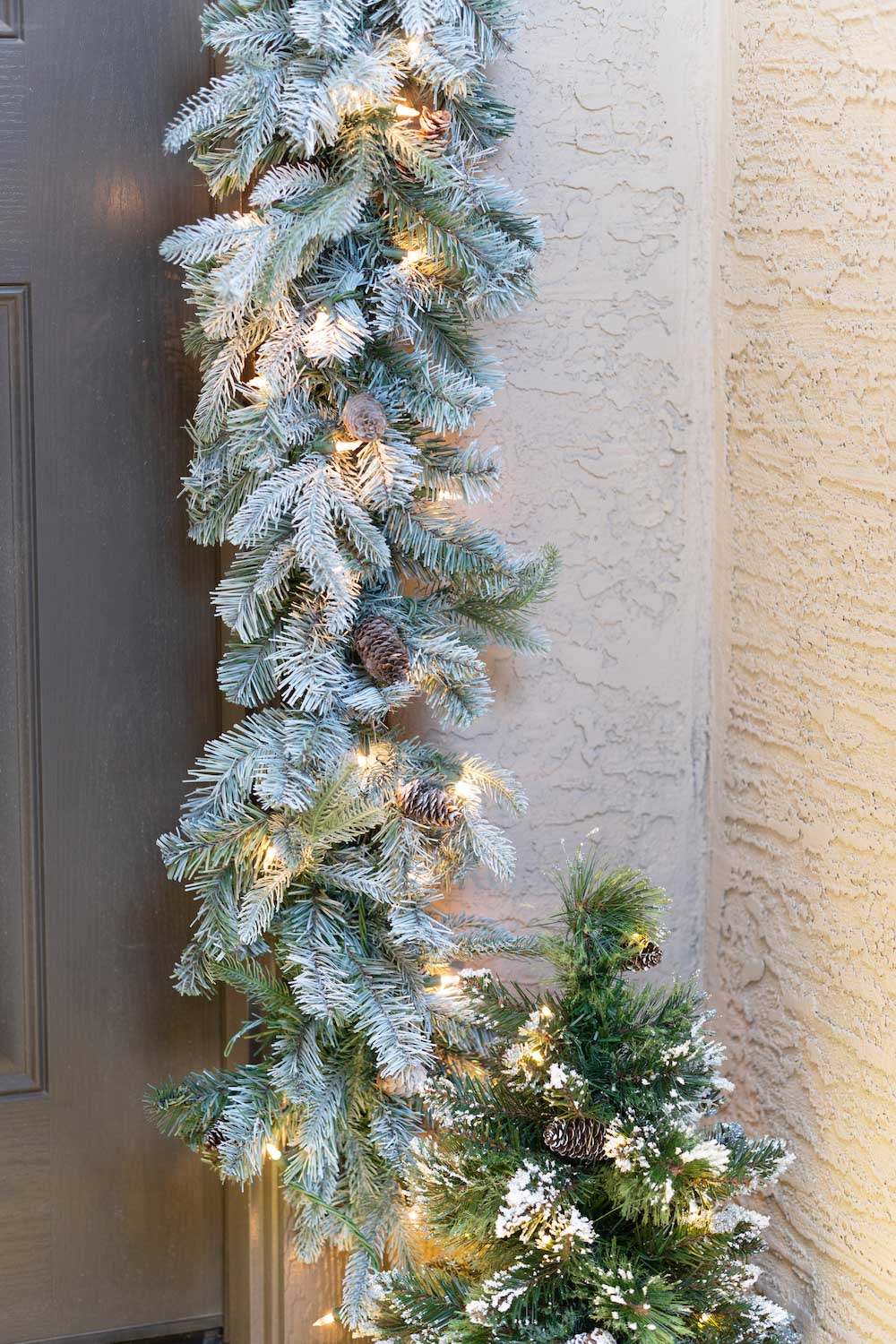 A front porch is styled with illuminated garland and a small, lit tree shot in corner