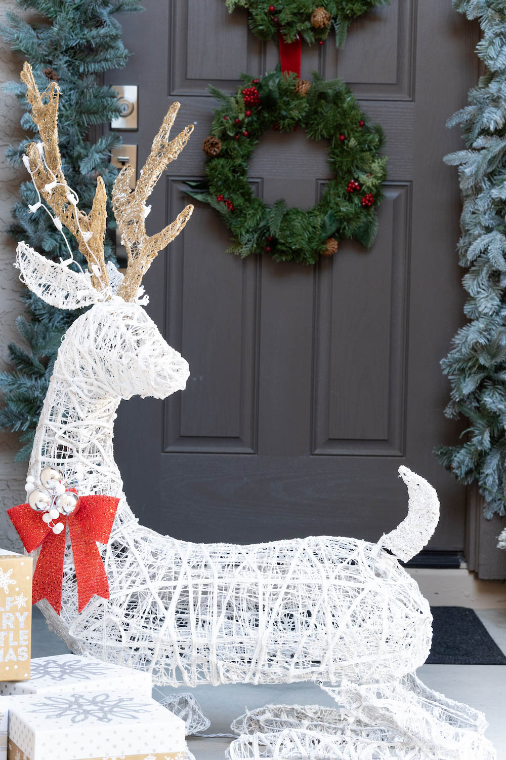 A front porch is styled with LED deer, presents, wreaths and garland