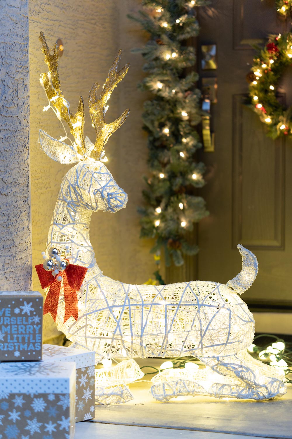 A front porch is styled with LED deer, presents, wreaths and garland shot in corner
