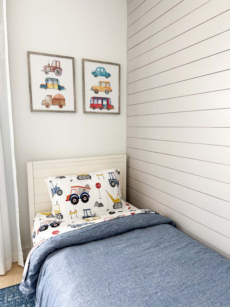 Twin bedding with two hanging car paintings in a kids room. 