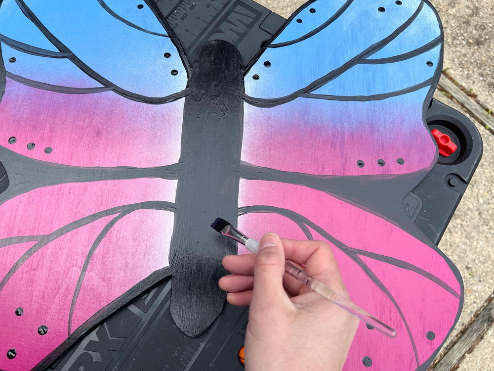 Person painting lines, dots, and details onto the painted butterfly.