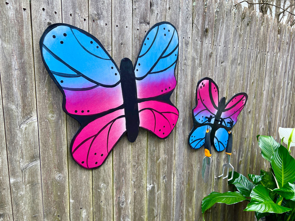 Left angle of two butterflies on a wooden fence, with gardening tools attached.