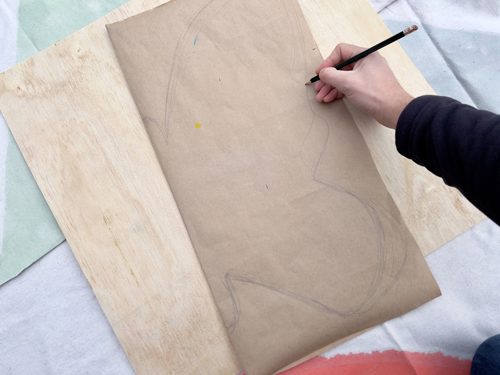 Person drawing an outline of half of a butterfly on top of a piece of plywood. 