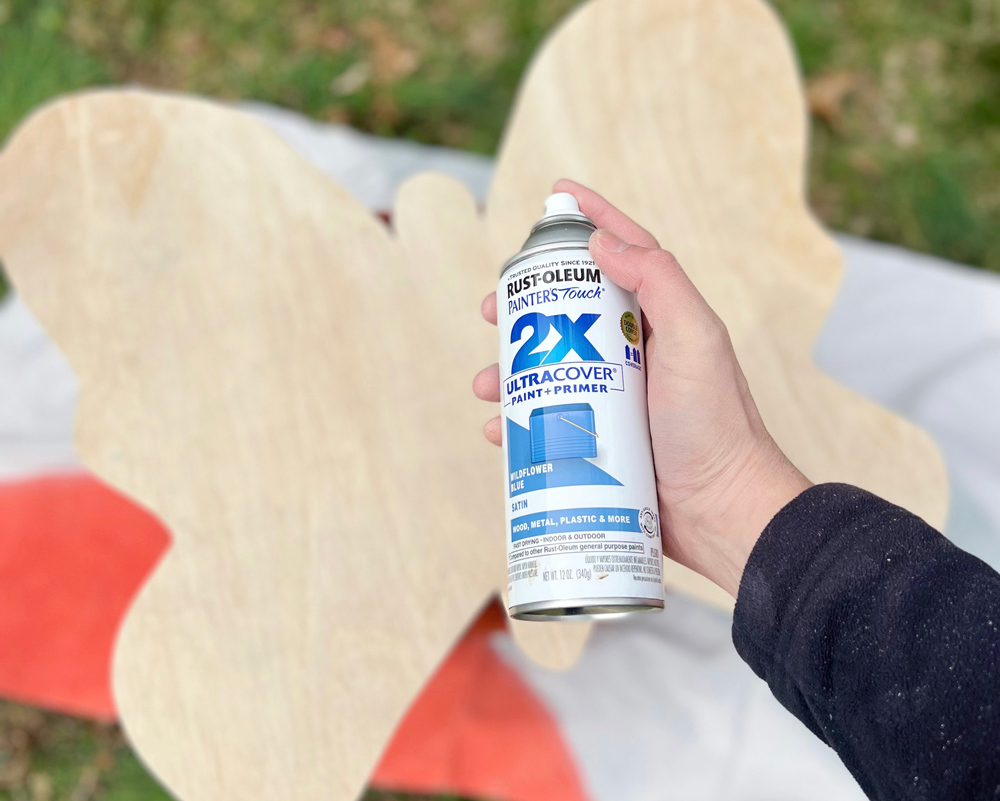 Person holding a can of Rustoleum primer over a plywood butterfly.