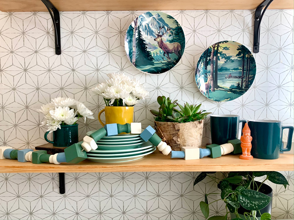 Shelves on a wall with plates, decor, and DIY Colorful Wooden Spring Garland strung across.