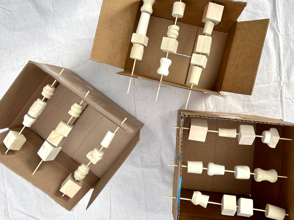 Spindle pieces strung with skewers over cardboard boxes.