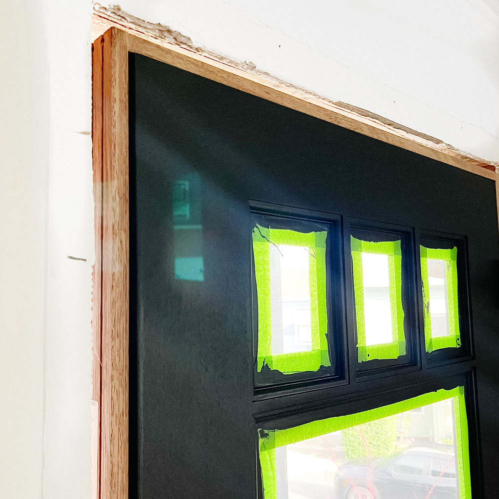 A door with green painter’s tape on glass and a wooden door frame.