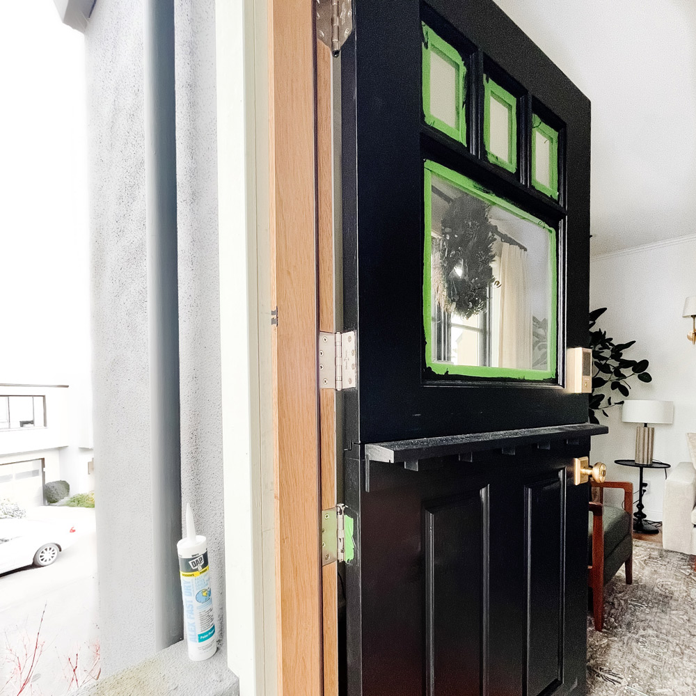 A full black Dutch door ajar in a doorway with green painter’s tape on top panel windows.