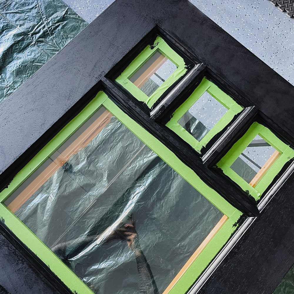 A door panel painted black with green painter’s tape on the windows.