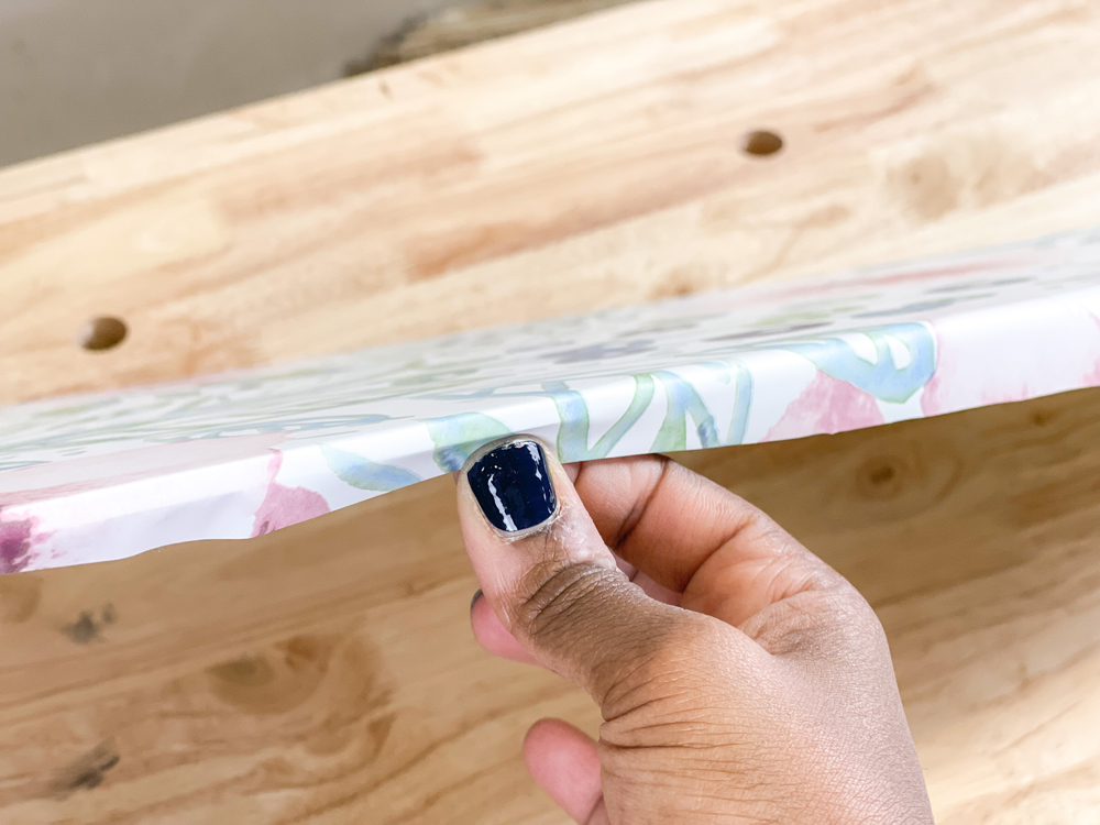 A woman's hand folding floral wallpaper around a piece of plywood A woman's hand folding floral wallpaper around a piece of plywood