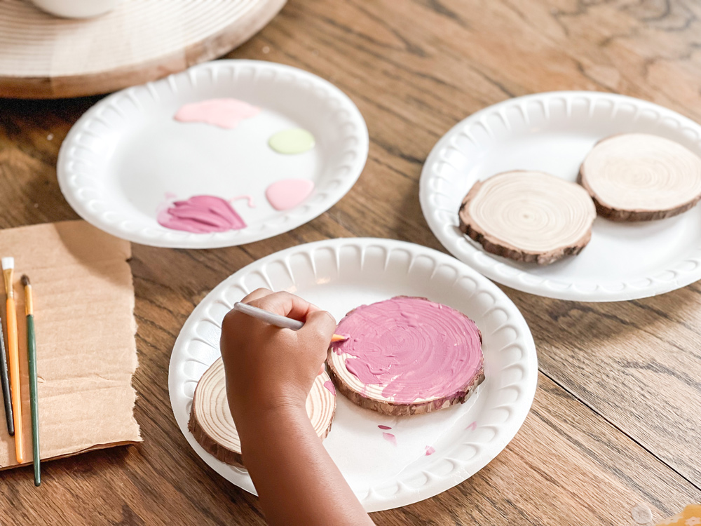 A child's hand painting round wood slices on a Styrofoam plate A child's hand painting round wood slices on a Styrofoam plate