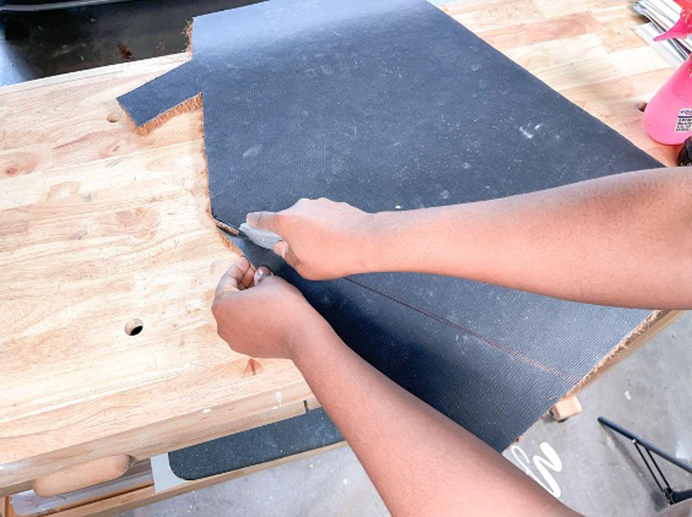 Hands using a box cutter to cut a doormat.