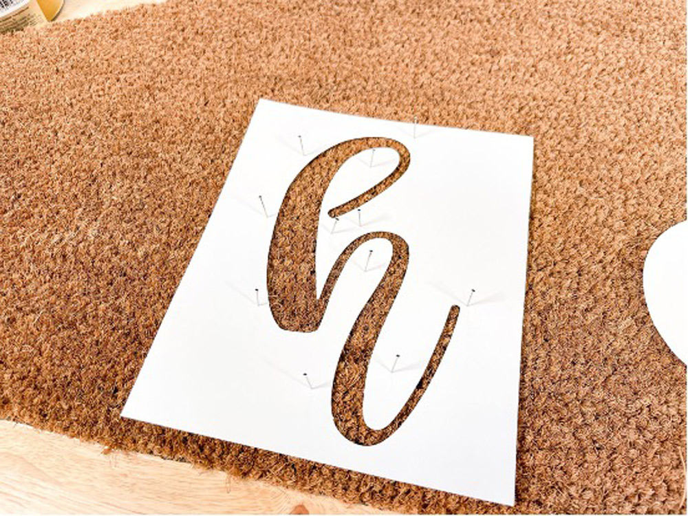 A calligraphic letter h stencil resting on a doormat.