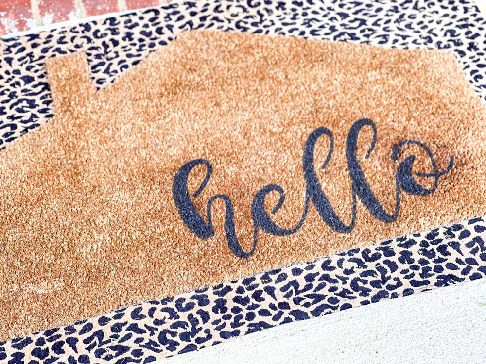 A completed DIY Welcome Mat on a doorstep layered on top of a cheetah print doormat.