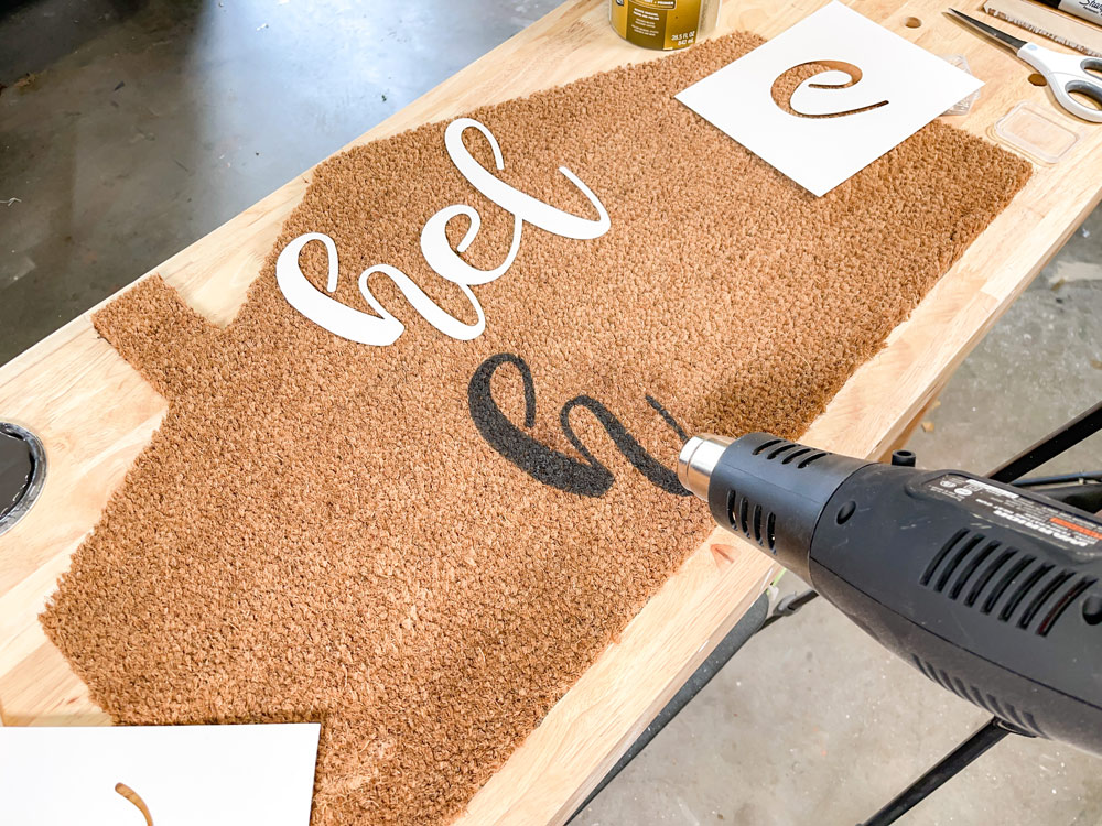 A heat gun being used on a painted letter on a doormat.