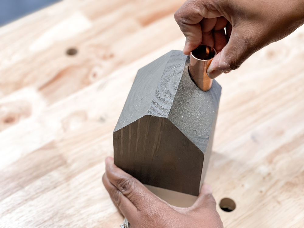 A hand placing a copper pipe into a DIY Wooden House Candle Holder