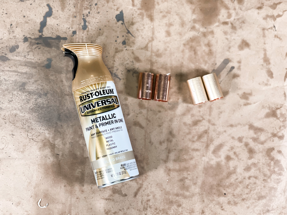 A bottle of gold spray paint next to two copper pipe pieces and two spray painted pipe pieces A bottle of gold spray paint next to two copper pipe pieces and two spray painted pipe pieces