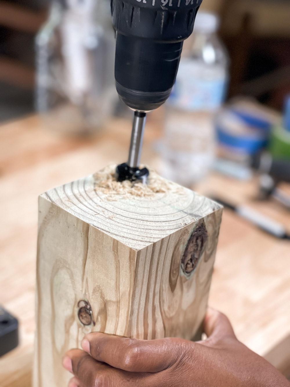 A hand holding a block of wood while a drill is used on the top