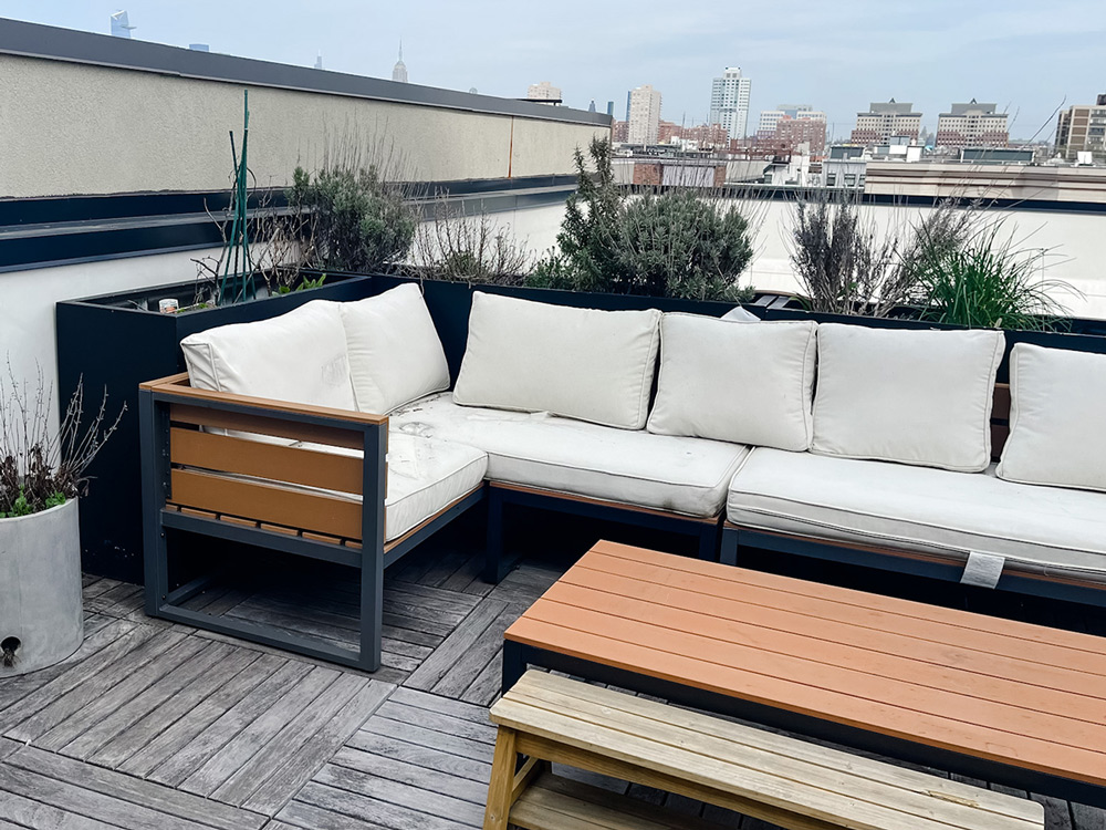 Rooftop seating with dull plants behind the furniture.