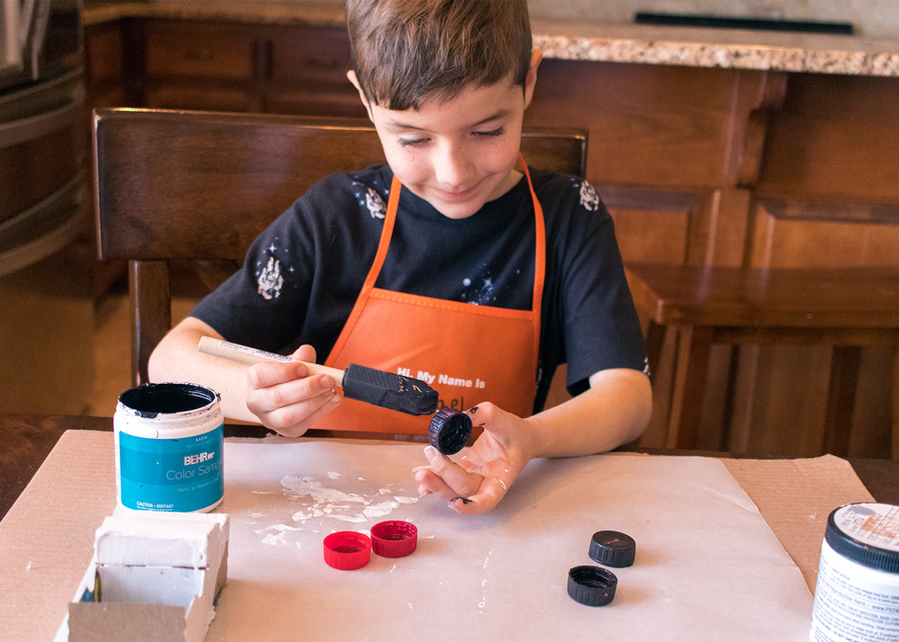 Shot of young boy painting bottle caps black