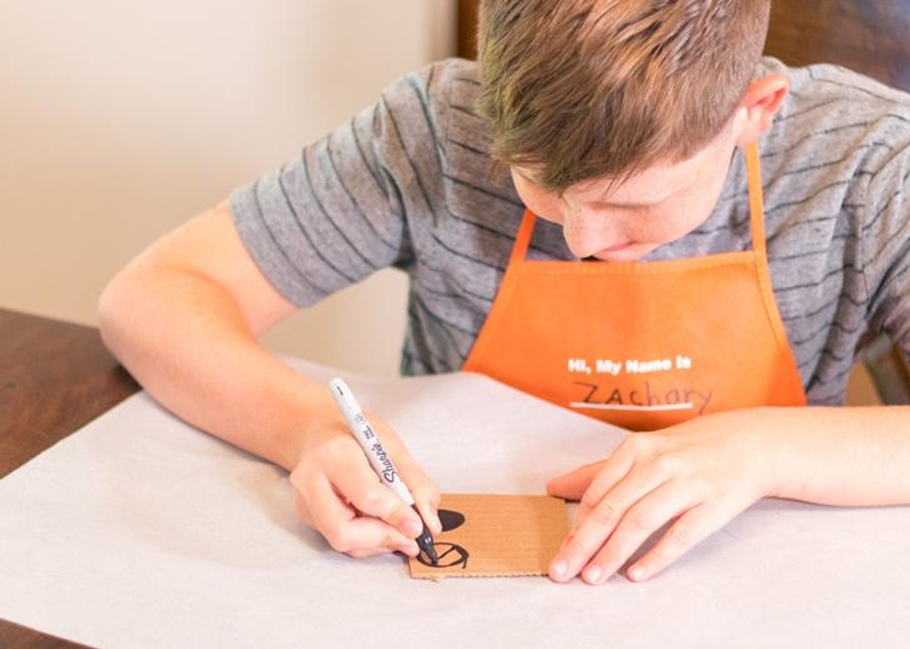 Boy drawing wheels on a piece of cardboard.