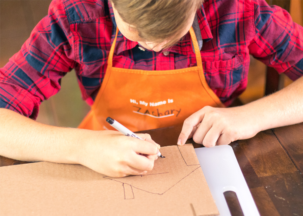 Boy drawing a house on cardboard.