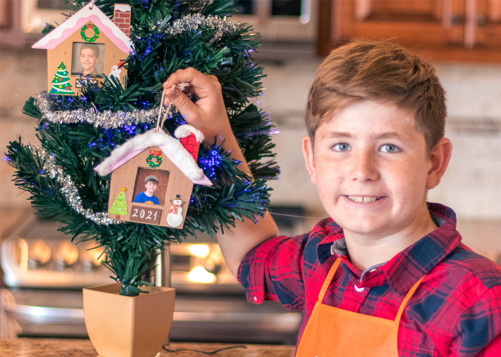 Boy hanging his house ornament on a mini Christmas tree.