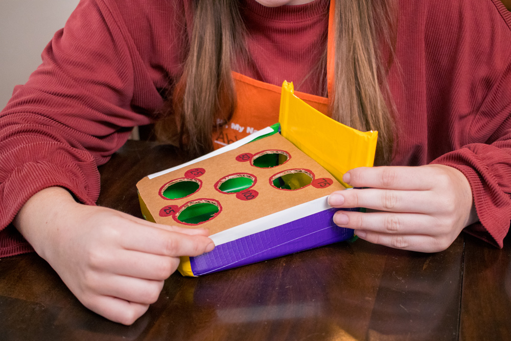 A girl applying colorful duct tape to a DIY Toss Game base.