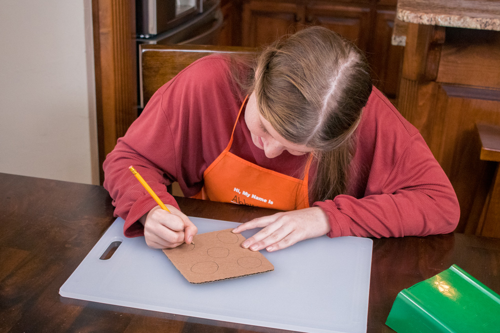 A girl drawing circles on cardboard with a pencil.