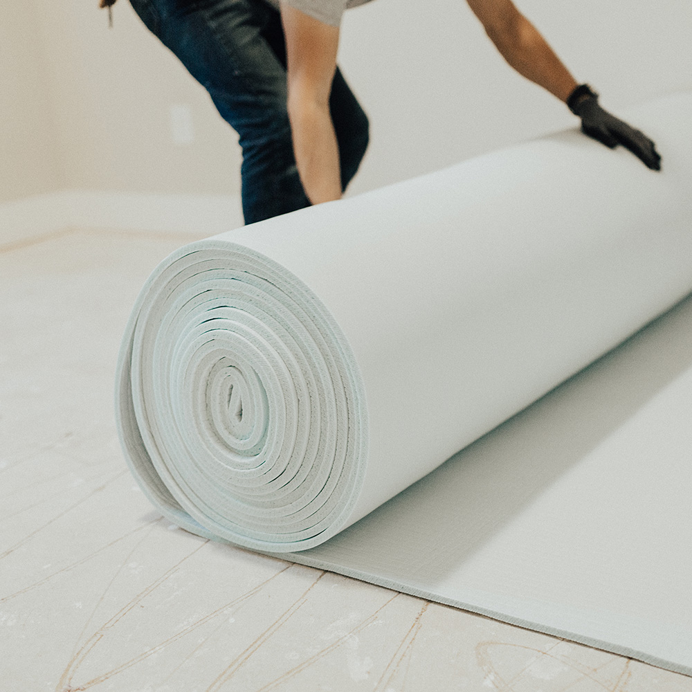 A man installs a roll of carpet padding.
