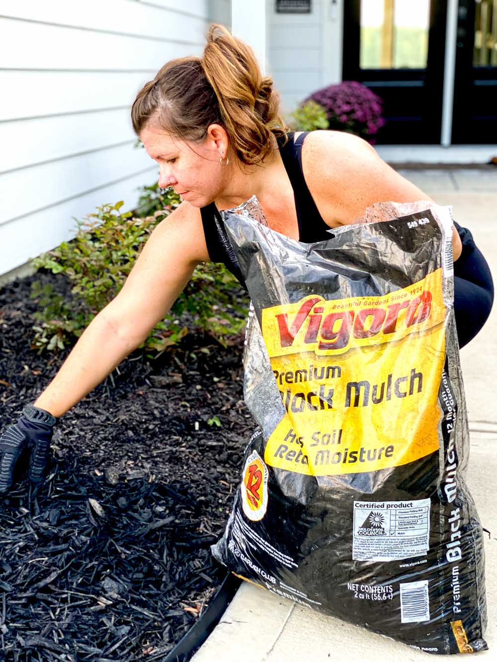 A woman placing premium black mulch from a bag.