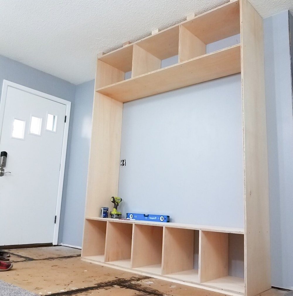 Light brown wood boards built into a pastel blue wall with a power drill and level sitting on the bench