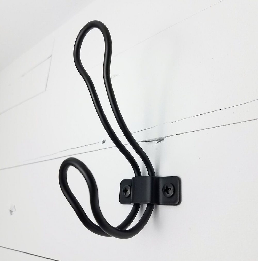 Close up of a black coat hook on a white painted board