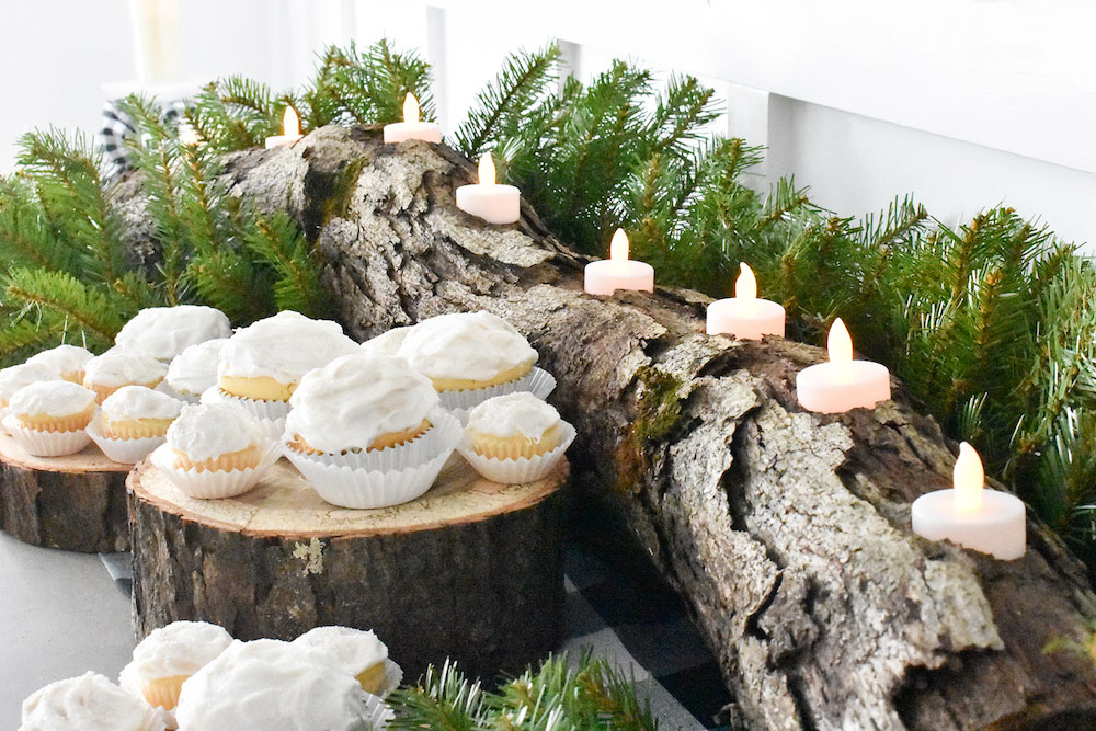 Cupcakes sitting on a log with tea light candles surrounded by greenery