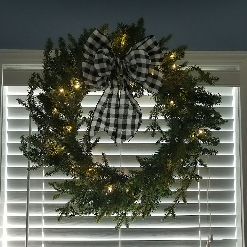 Christmas wreath with black and white bow hanging in a window 