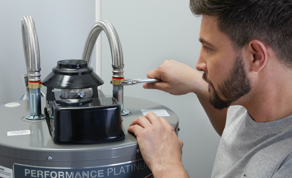 A person adjusts a water heater with a wrench.