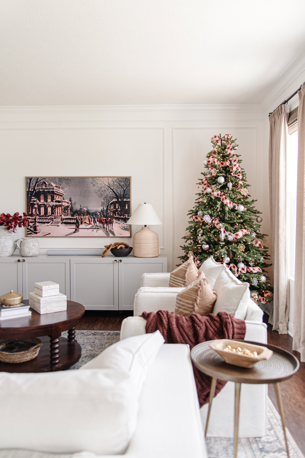 Living room featuring traditional green Christmas tree with plaid ribbon. 