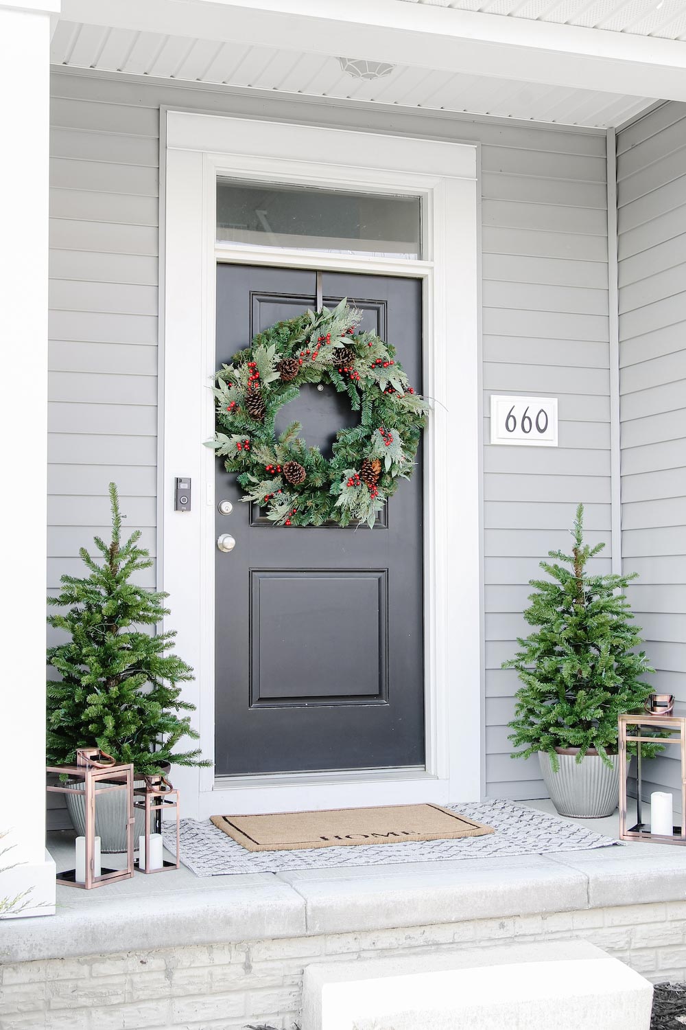 A front porch is styled with oversized holiday wreath, generic trees and lanterns with house numbers visible. 