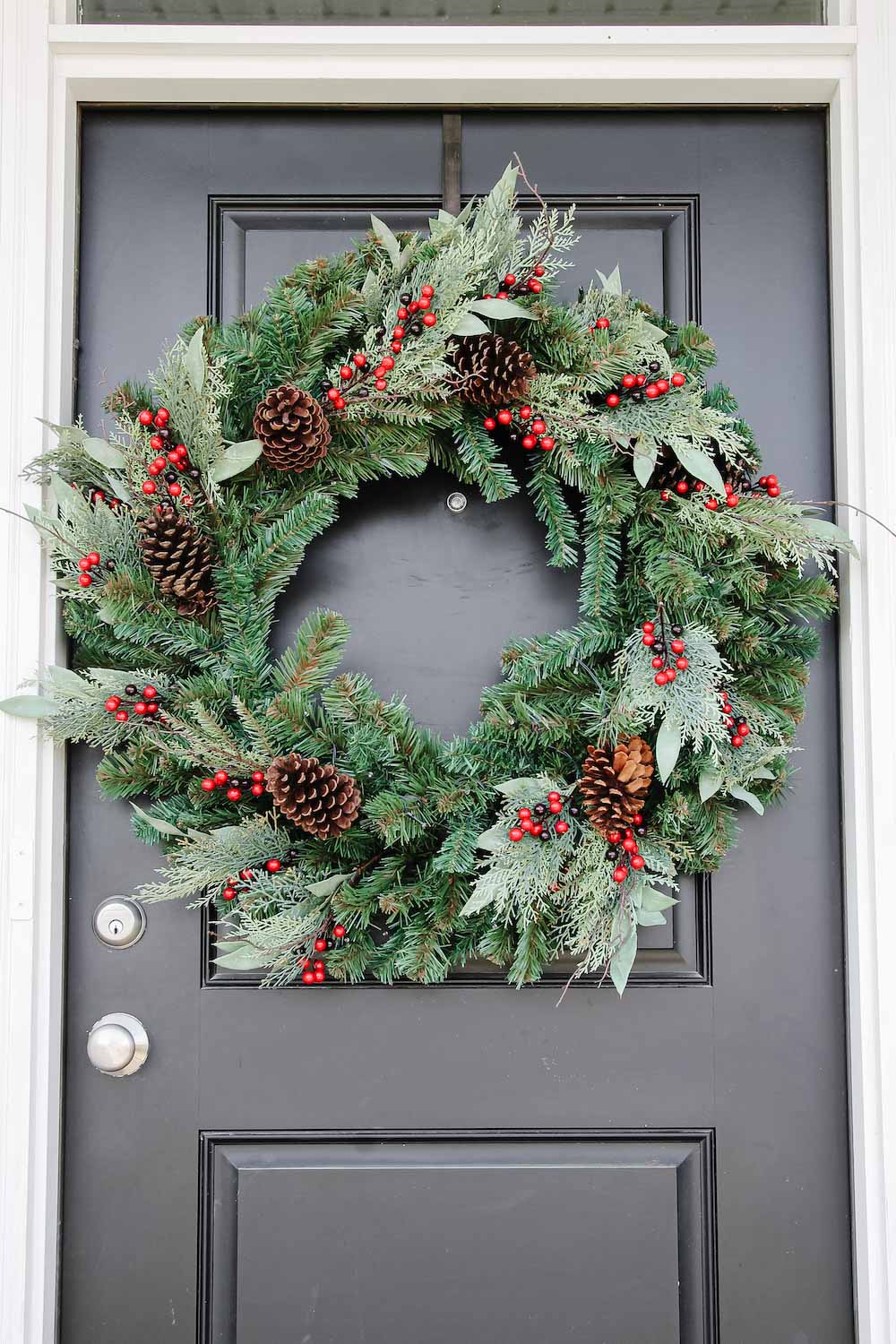  An oversized holiday wreath with pine cones and red berries hanging on black door