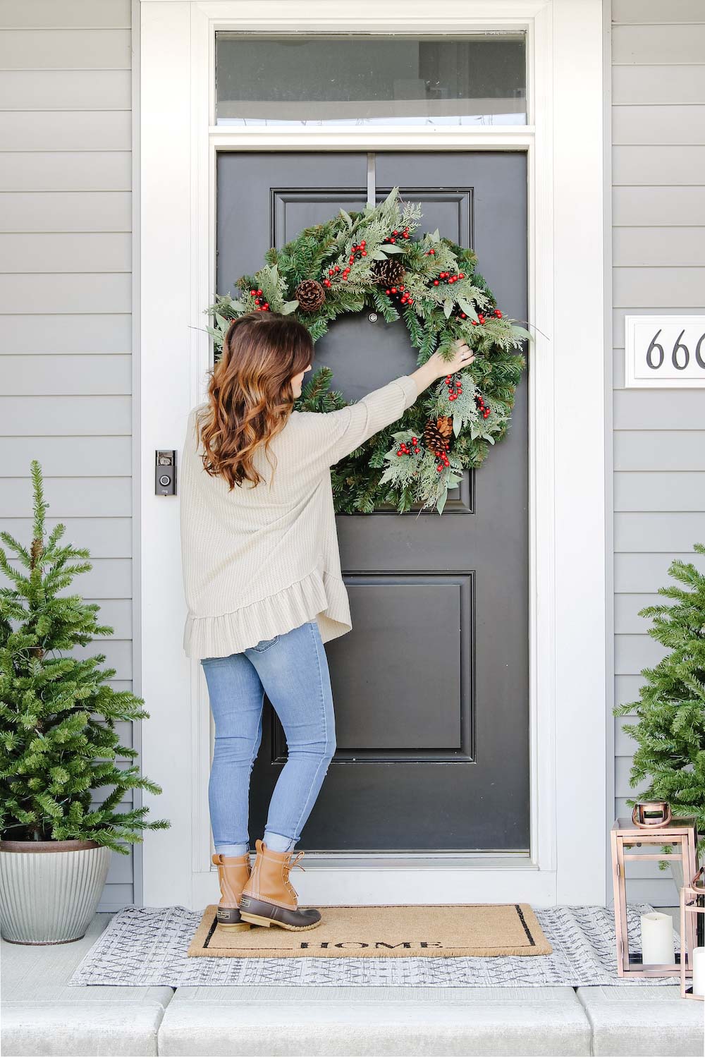 A woman styles an oversized holiday wreath on a front door.