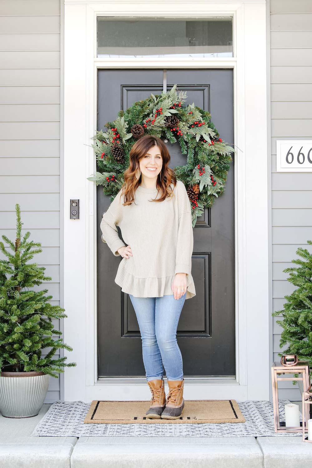 A woman standing on porch style for holidays with oversized holiday wreath and porch trees with lanterns