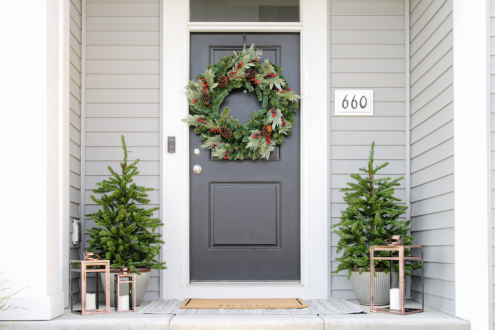 A front porch styled with oversized holiday wreath, porch trees, and lanterns.