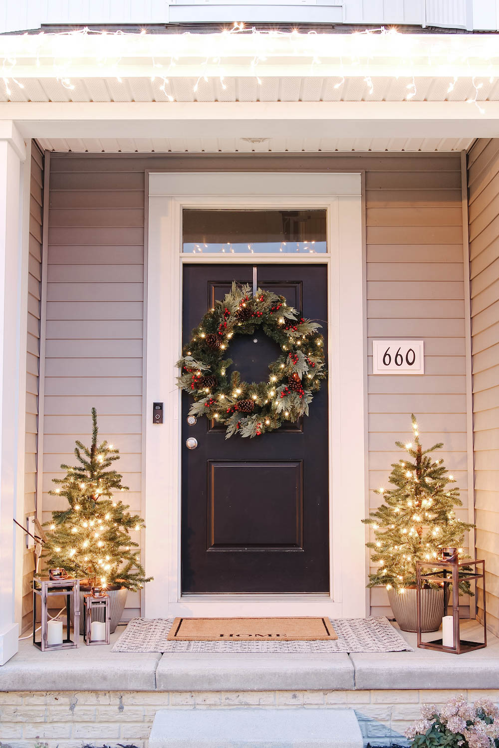 A front porch styled for the holidays with illuminated porch trees and oversized wreath